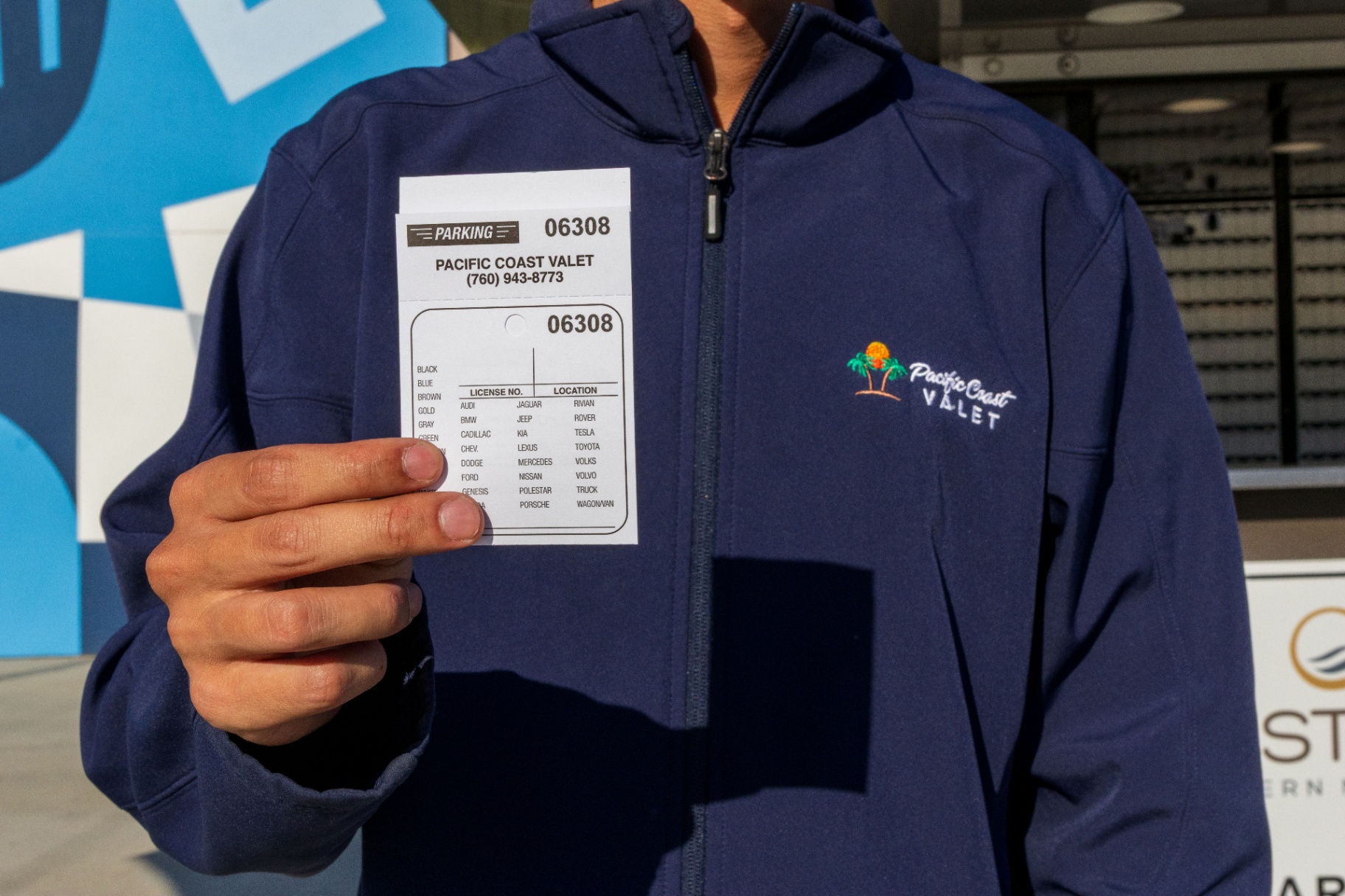 Pacific Coast Valet attendant in a branded jacket holding a numbered valet ticket